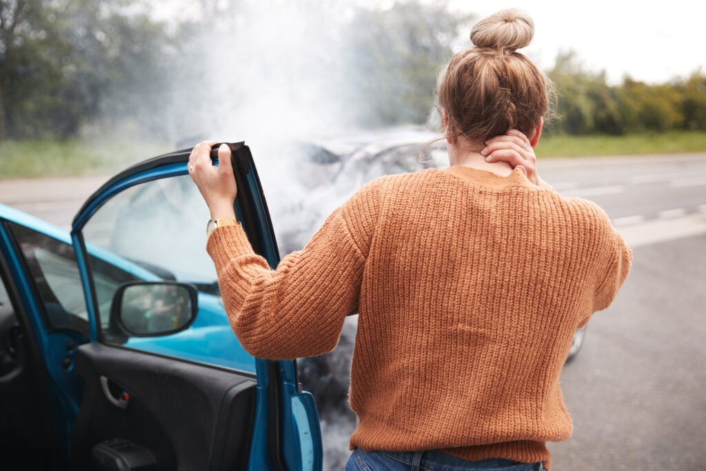 Mujer saliendo de un coche frotándose el cuello con dolor después de un accidente de coche
